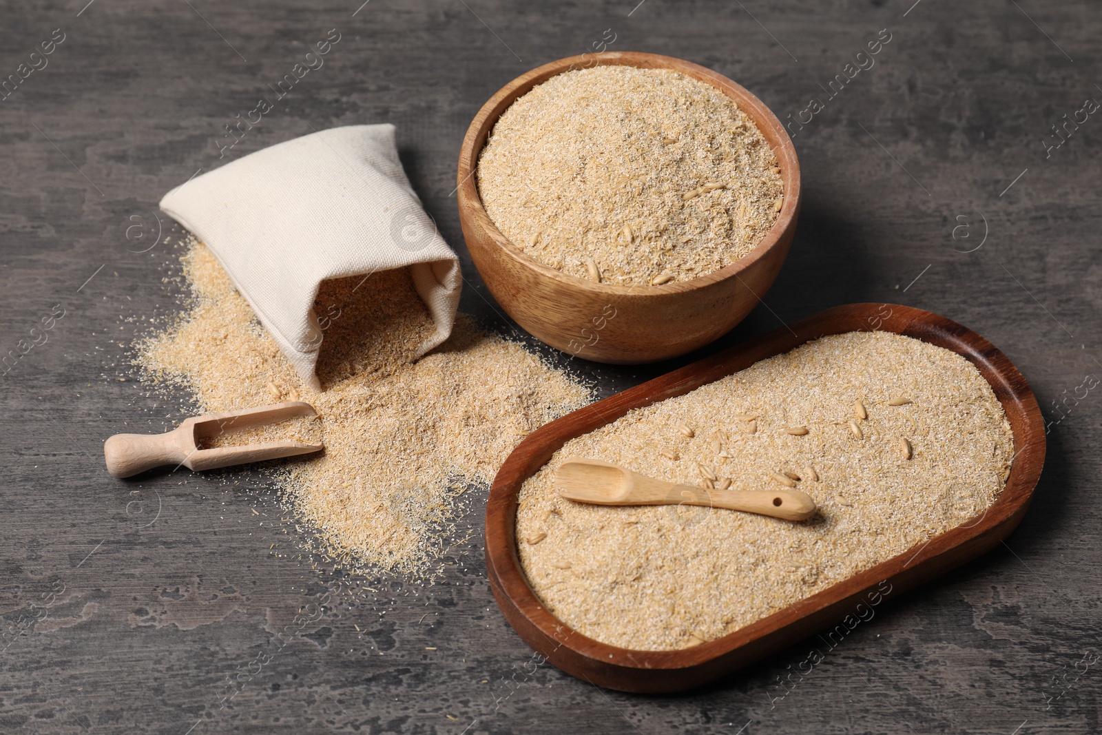 Photo of Oat bran in bowl, spoon, scoop and burlap bag on grey table