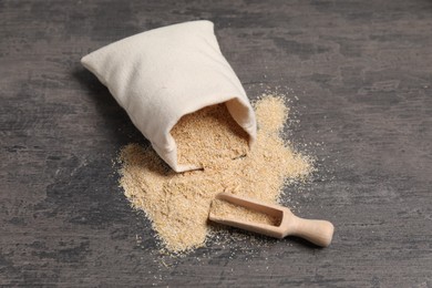 Photo of Oat bran in burlap bag and wooden scoop on grey table