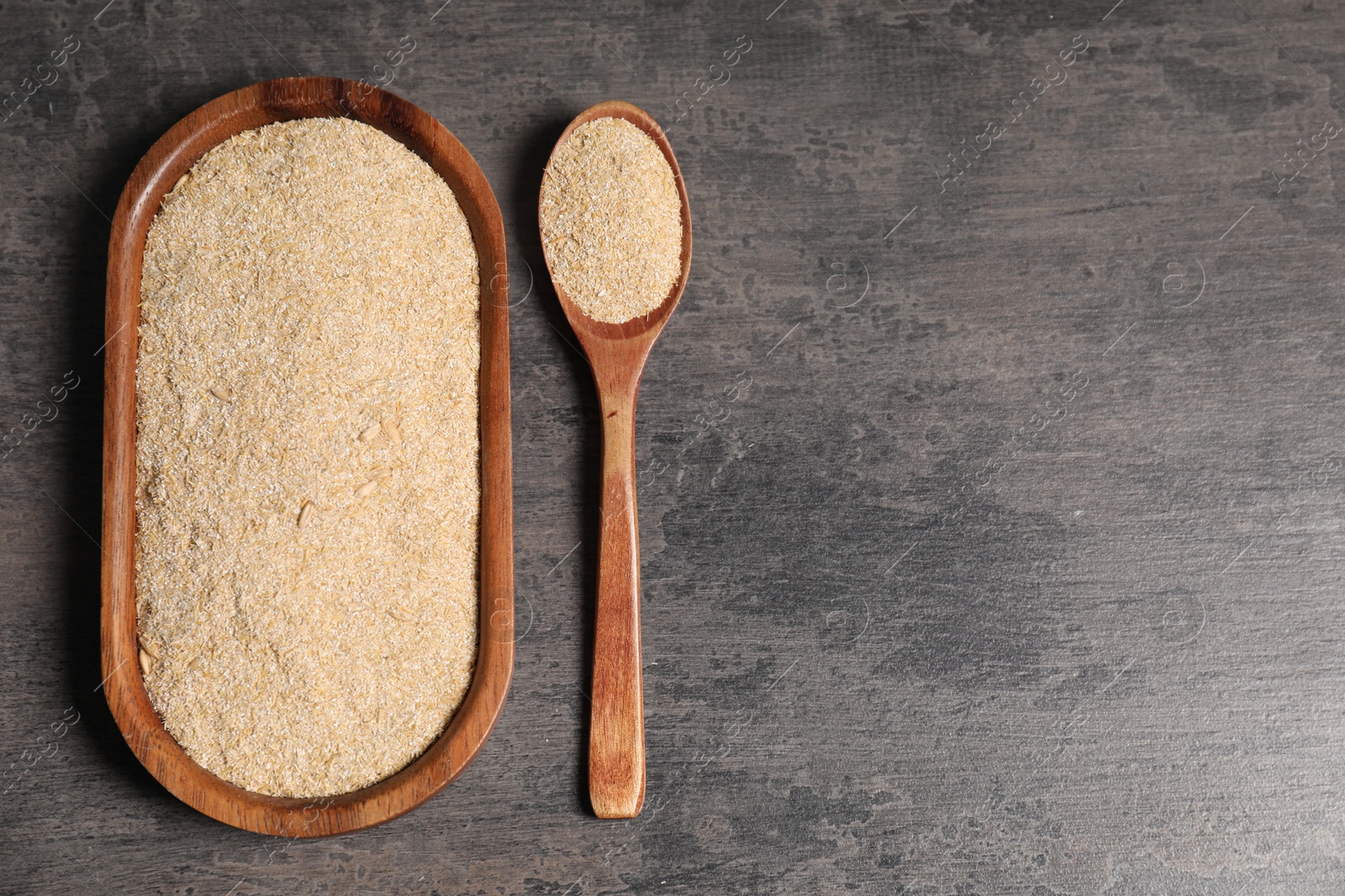 Photo of Oat bran in wooden spoon and plate on grey table, top view. Space for text