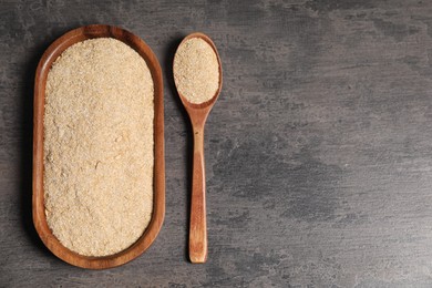 Photo of Oat bran in wooden spoon and plate on grey table, top view. Space for text