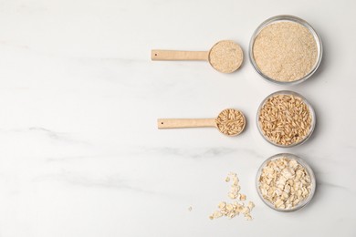 Photo of Oat bran, grains and flakes on white marble table, flat lay. Space for text