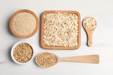 Oat bran, grains and flakes on white marble table, flat lay