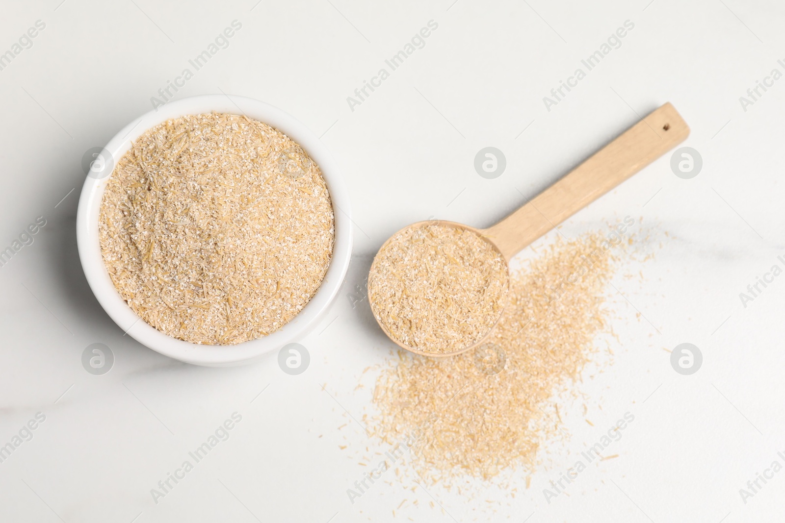 Photo of Oat bran in bowl and spoon on white marble table, top view