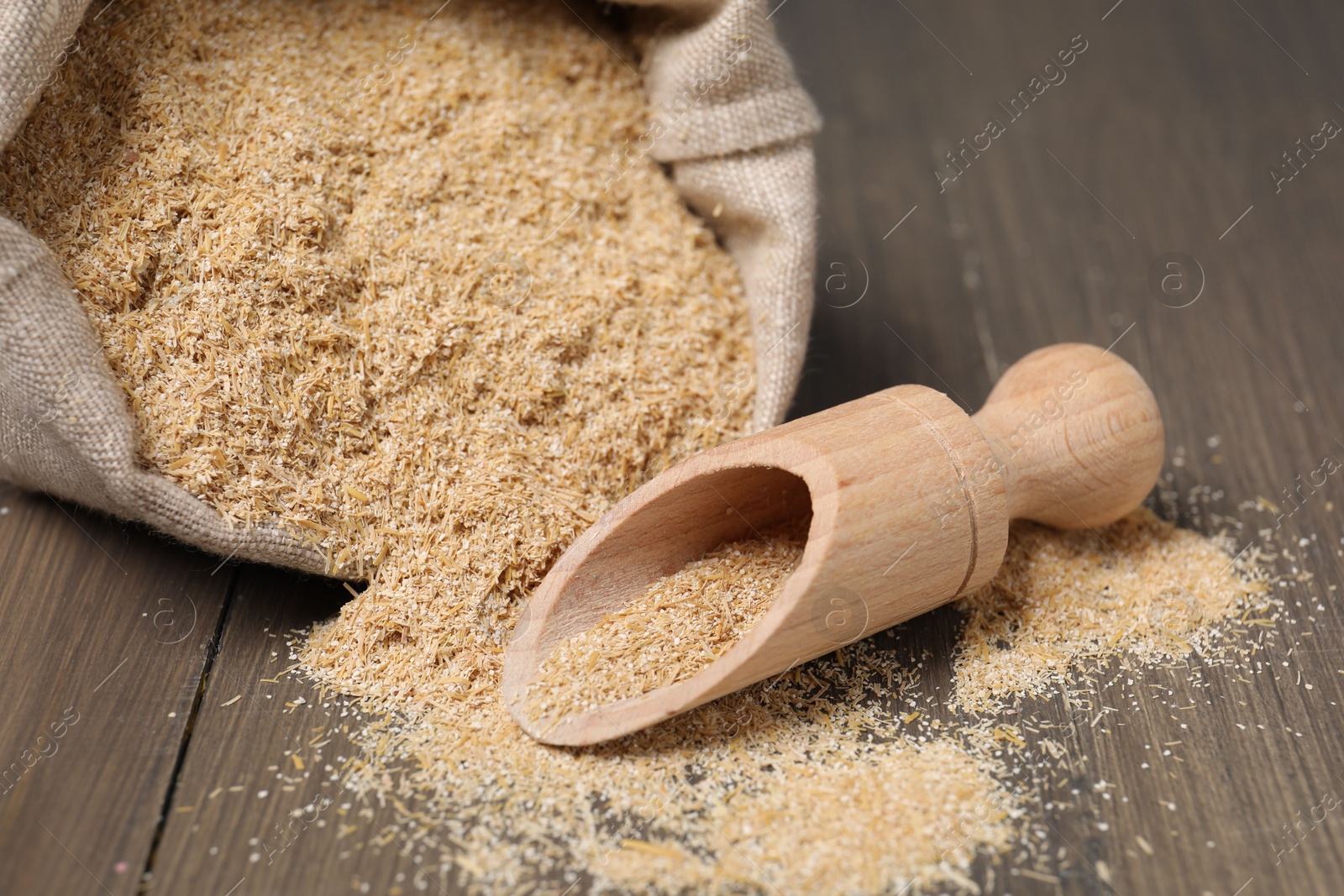 Photo of Oat bran in burlap bag and scoop on wooden table, closeup