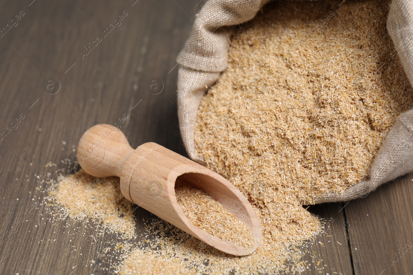 Photo of Oat bran in burlap bag and scoop on wooden table, closeup