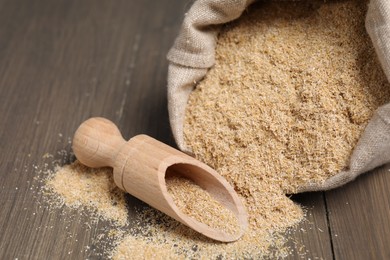 Photo of Oat bran in burlap bag and scoop on wooden table, closeup