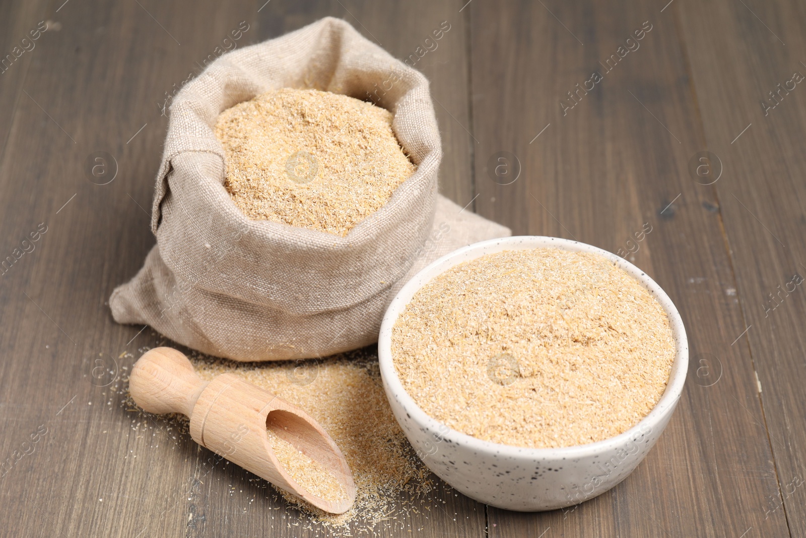 Photo of Oat bran in bowl, scoop and burlap bag on wooden table