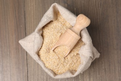 Photo of Oat bran in burlap bag and scoop on wooden table, top view