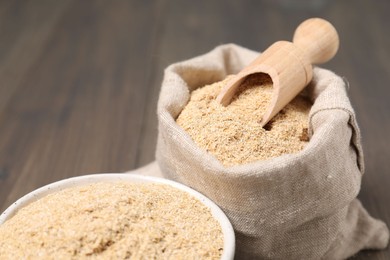 Photo of Oat bran in burlap bag, bowl and scoop on table, closeup