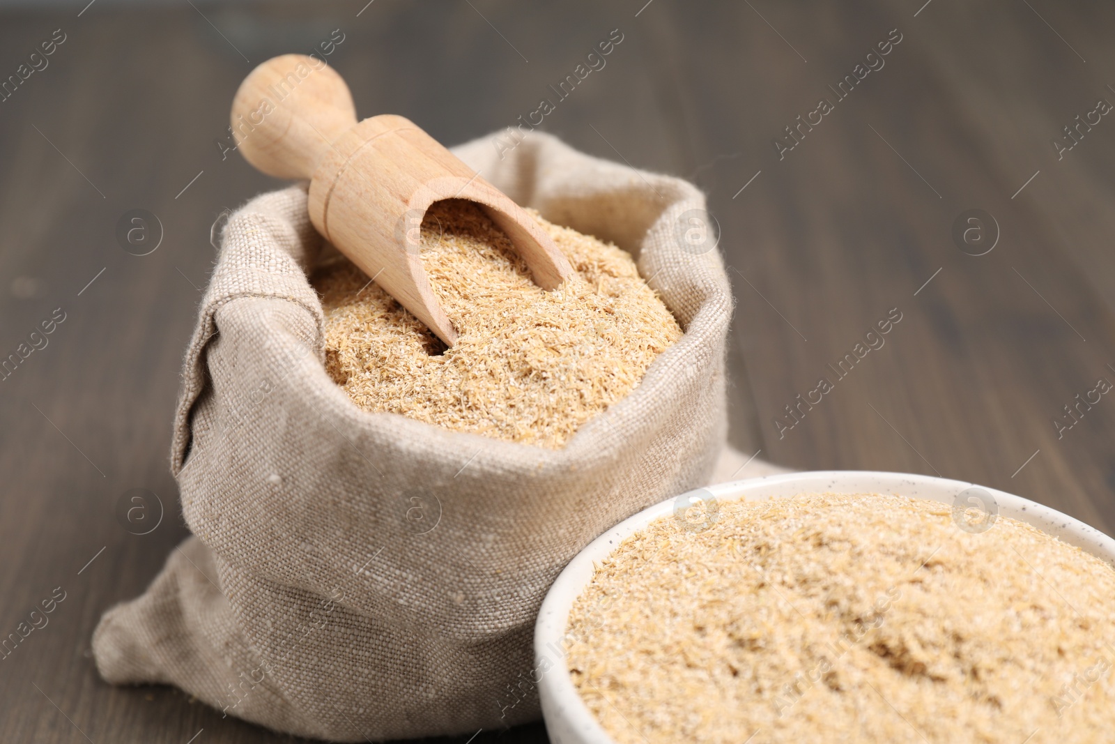 Photo of Oat bran in burlap bag, bowl and scoop on wooden table, closeup