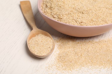 Photo of Oat bran in bowl and spoon on light wooden table, closeup