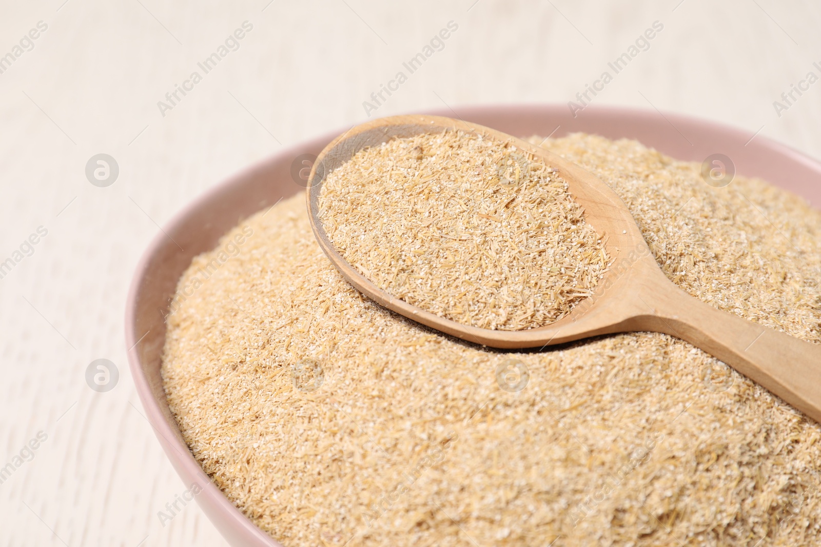 Photo of Oat bran in bowl and spoon on light table, closeup