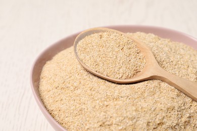 Photo of Oat bran in bowl and spoon on light table, closeup