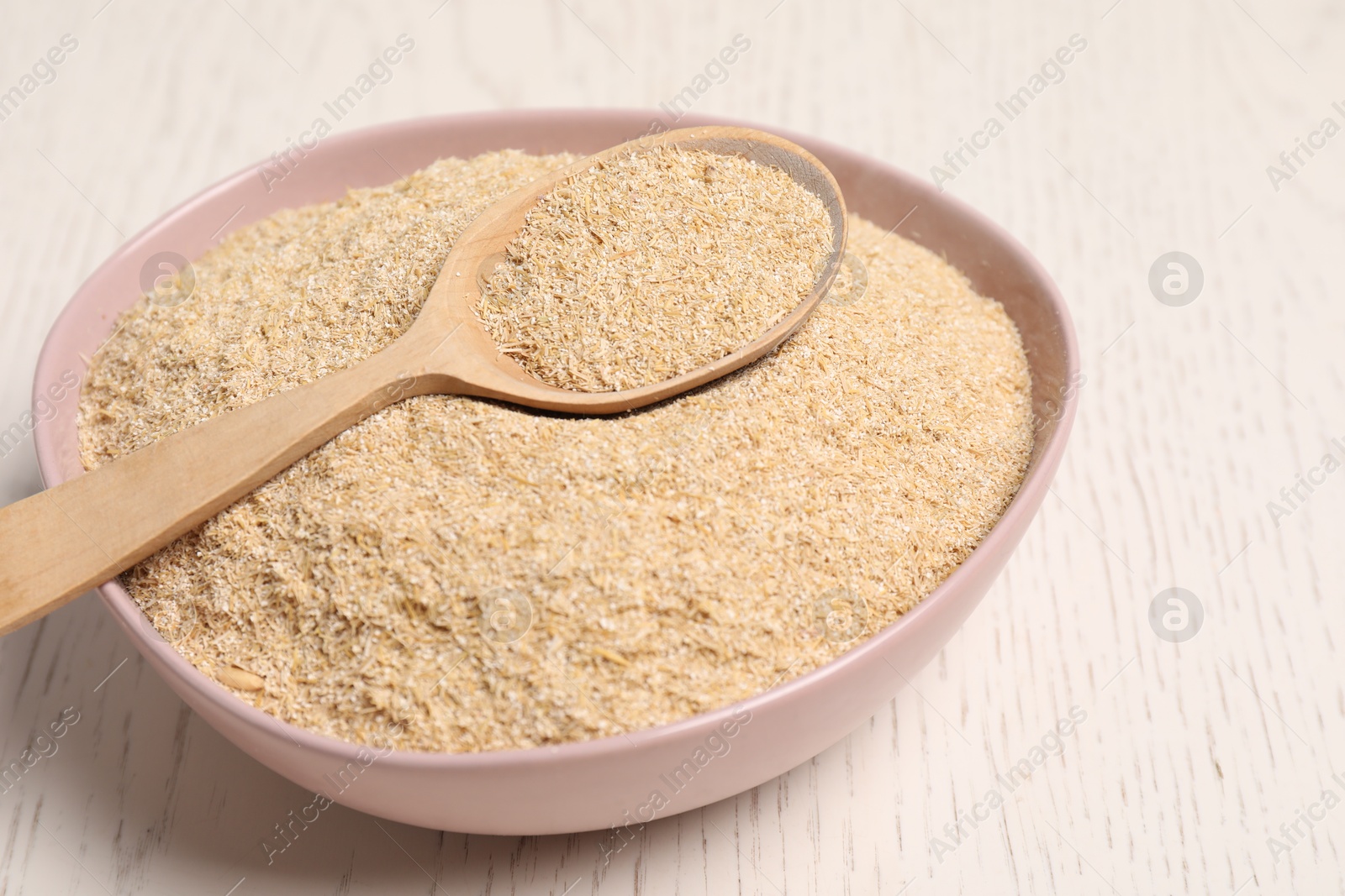 Photo of Oat bran in bowl and spoon on light wooden table, closeup