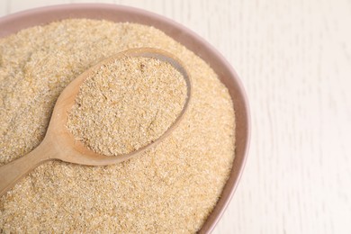 Photo of Oat bran in bowl and spoon on light table, closeup