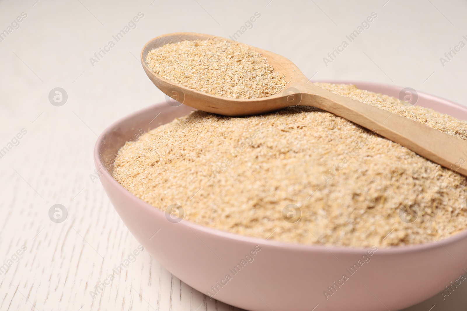 Photo of Oat bran in bowl and spoon on light wooden table, closeup