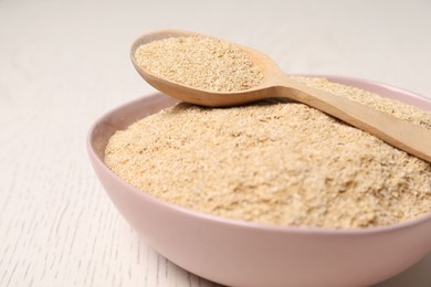 Photo of Oat bran in bowl and spoon on light wooden table, closeup