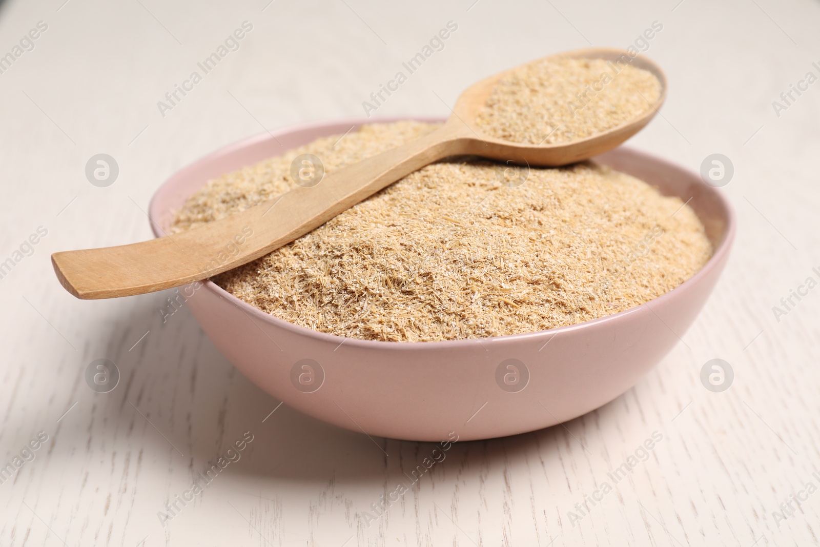 Photo of Oat bran in bowl and spoon on light wooden table, closeup