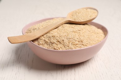 Photo of Oat bran in bowl and spoon on light wooden table, closeup