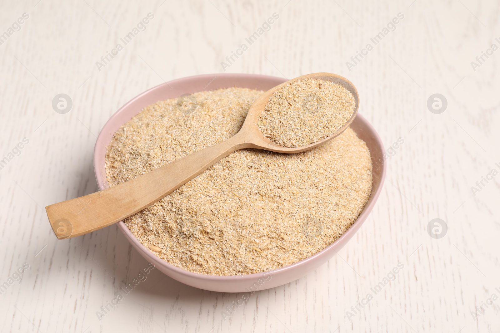 Photo of Oat bran in bowl and spoon on light wooden table, closeup