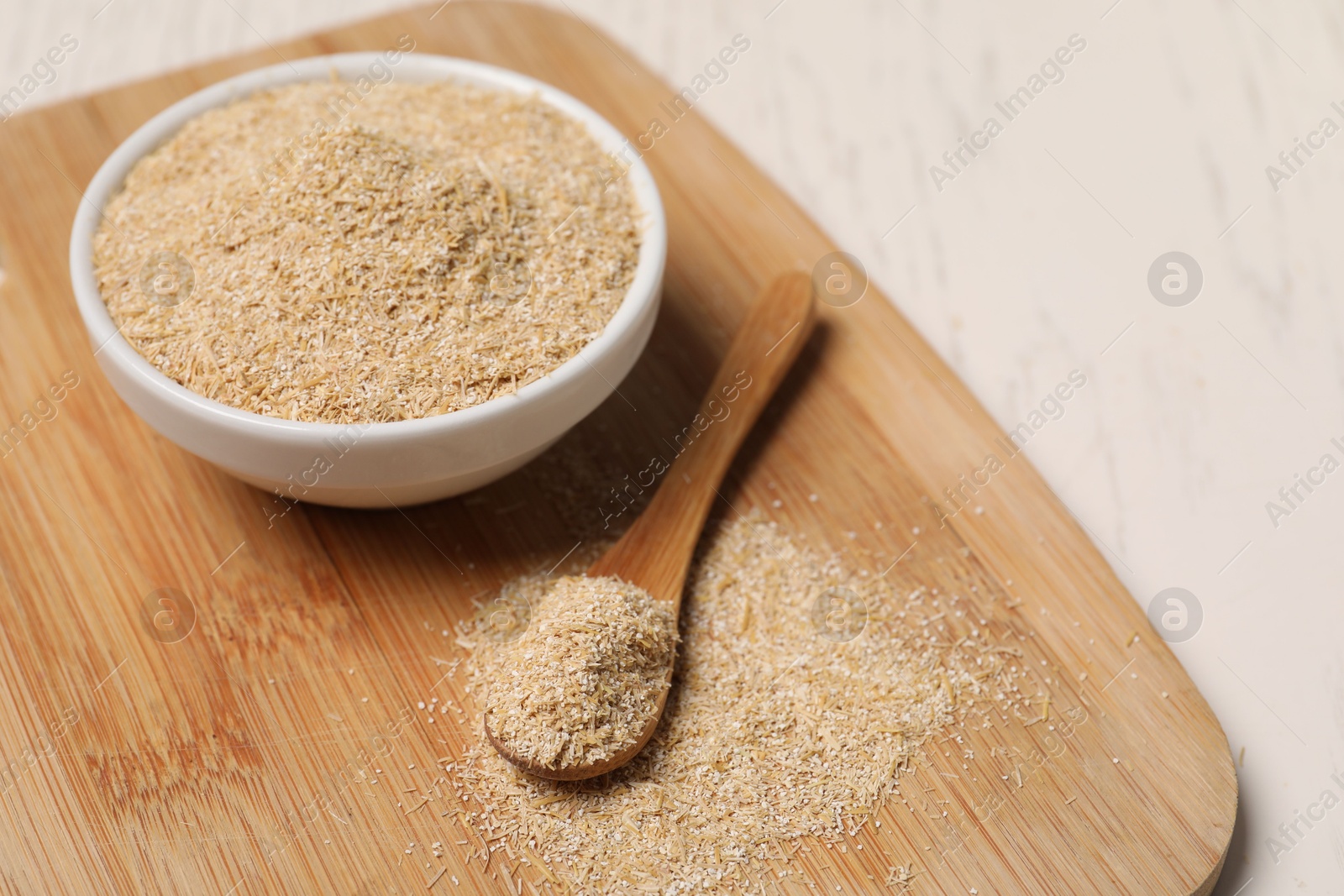 Photo of Oat bran in bowl and spoon on light table, closeup