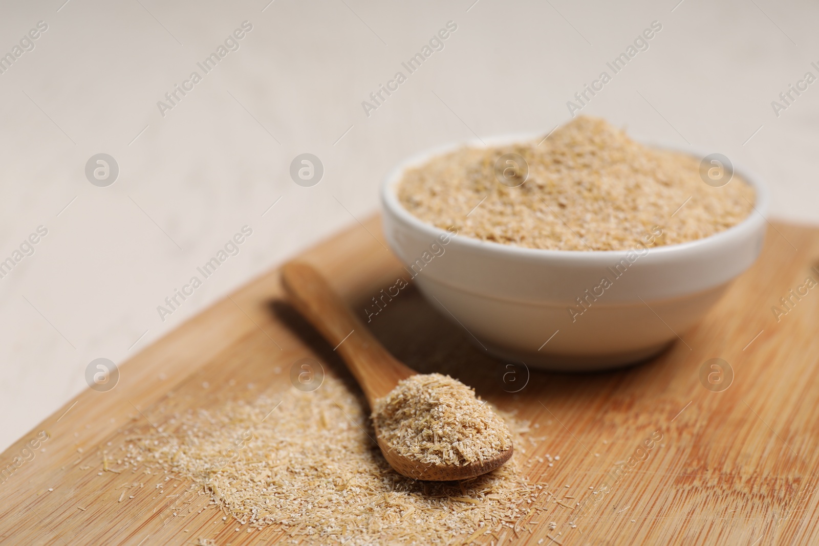 Photo of Oat bran in bowl and spoon on light table, closeup