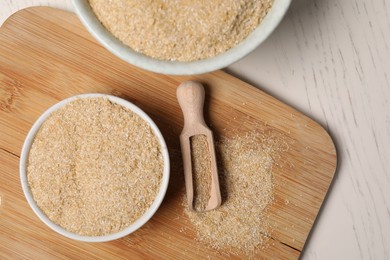 Oat bran in bowls and scoop on light wooden table, top view