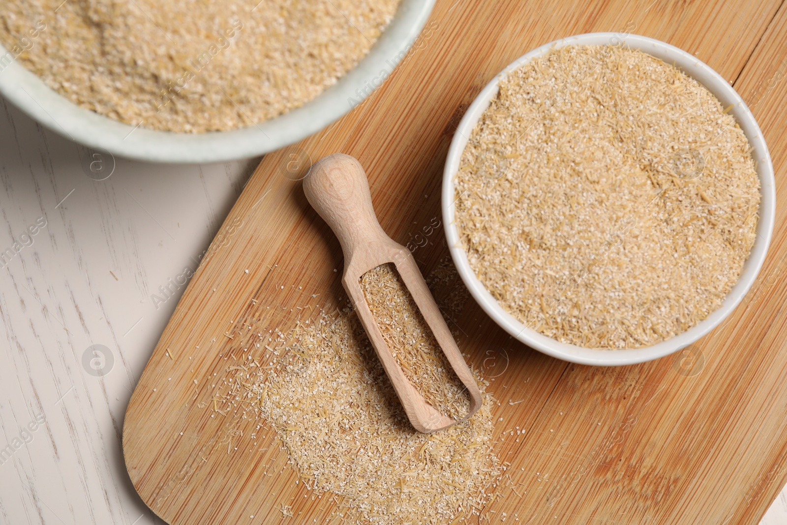 Photo of Oat bran in bowls and scoop on light wooden table, top view