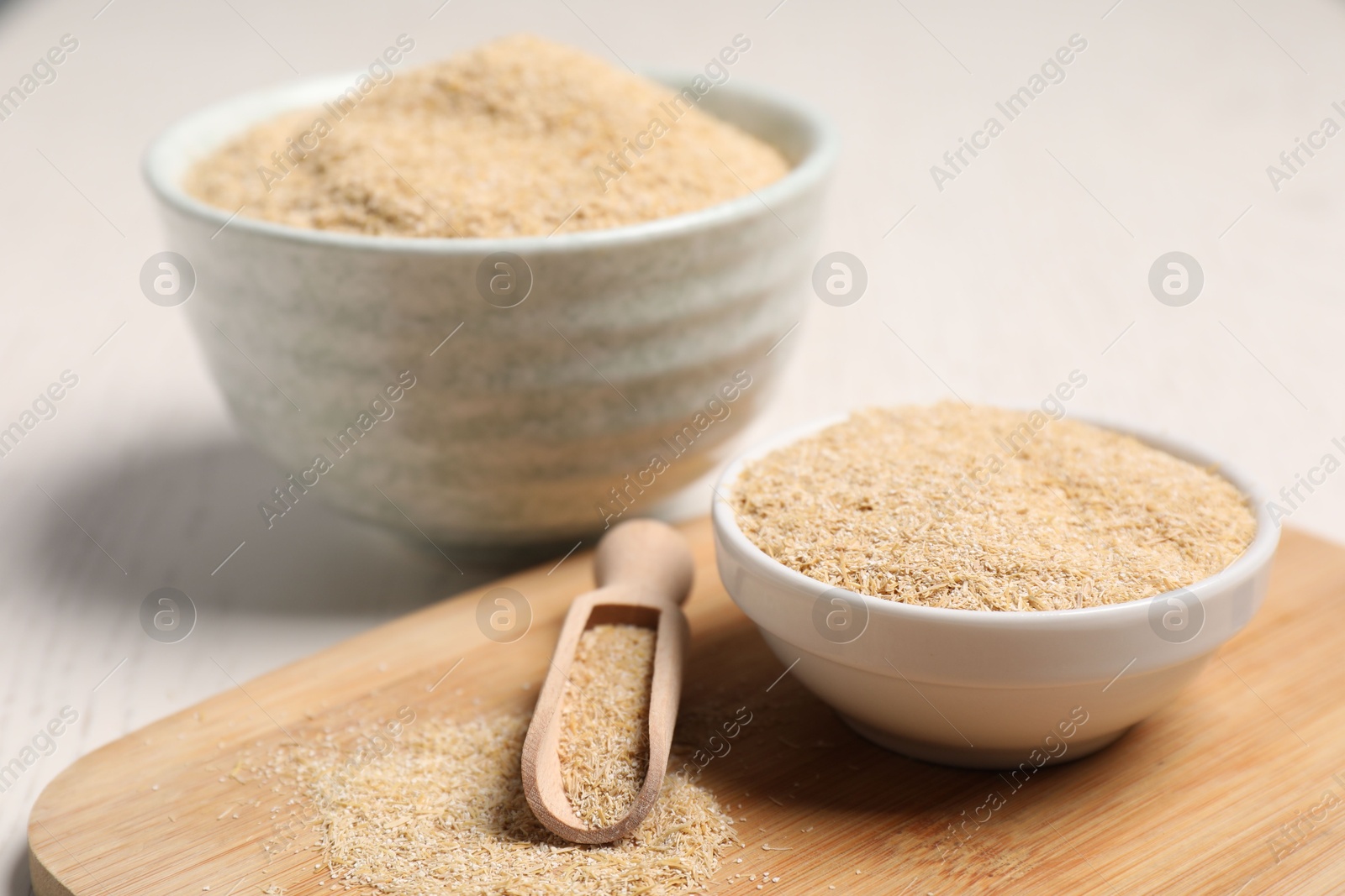 Photo of Oat bran in bowls and scoop on light table, closeup