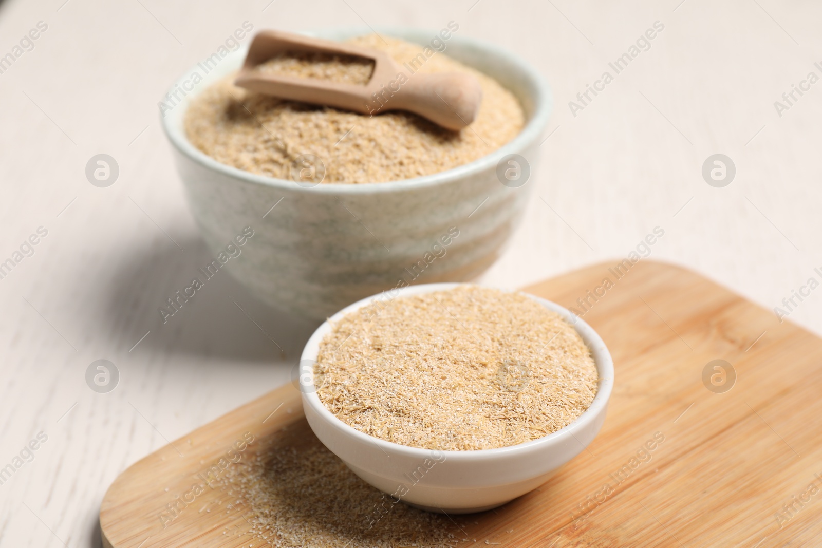 Photo of Oat bran in bowls and scoop on light table, closeup