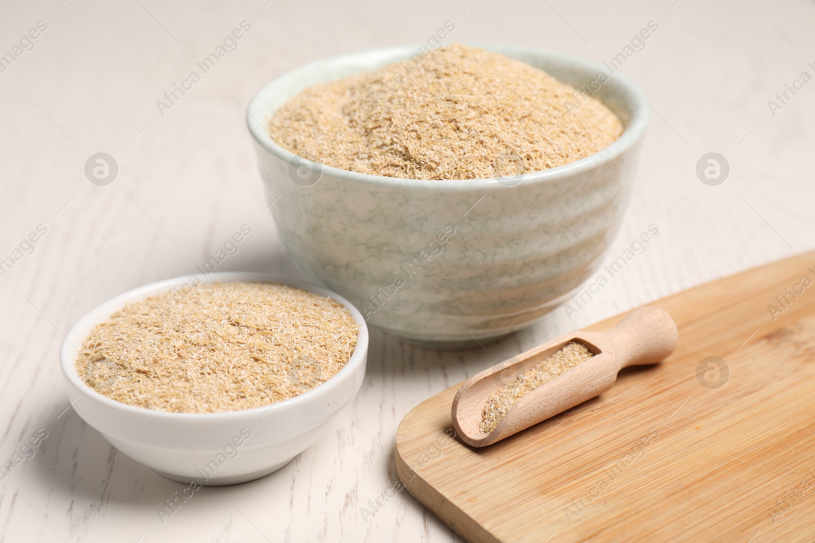 Photo of Oat bran in bowls and scoop on light wooden table, closeup