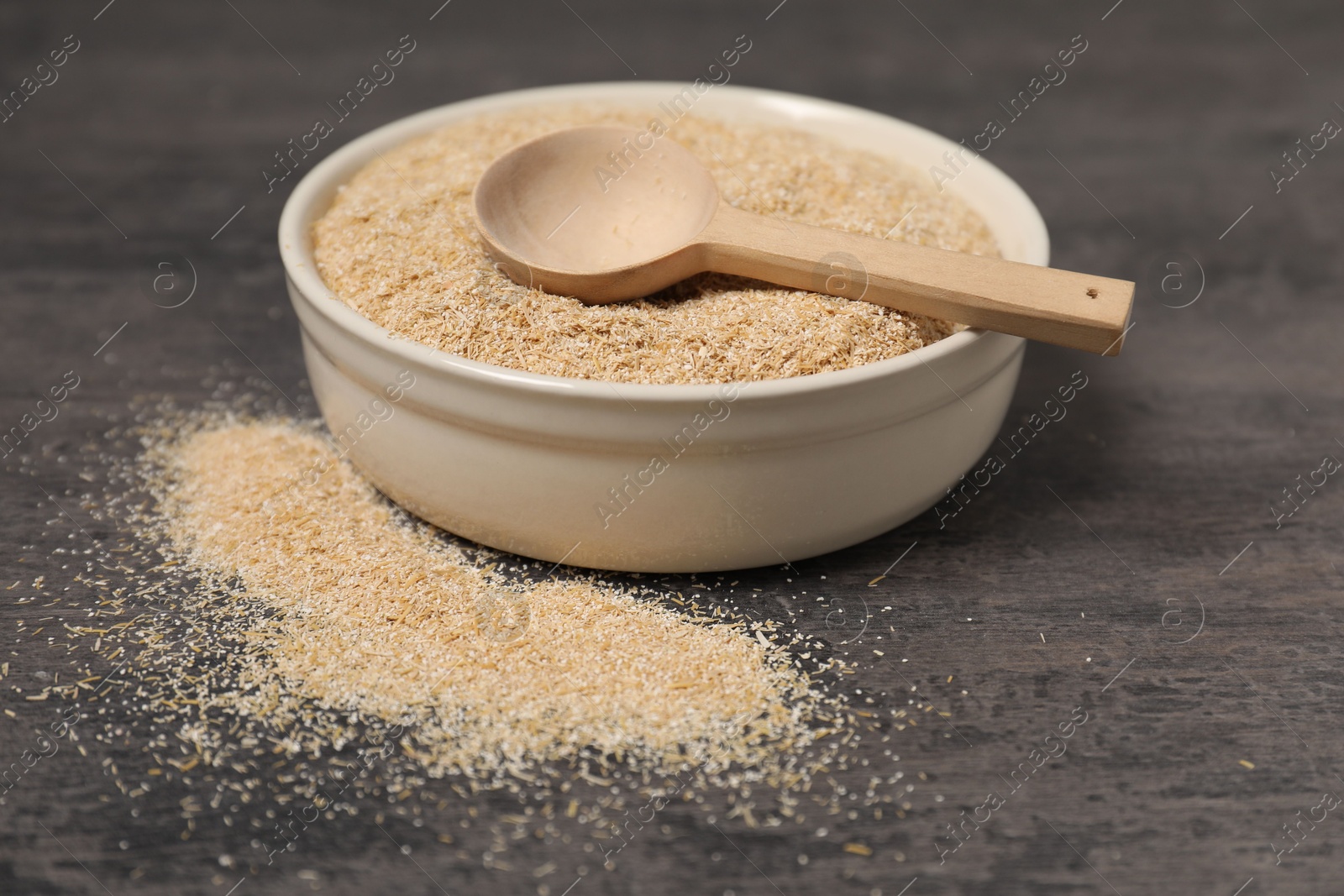 Photo of Oat bran in bowl and spoon on grey table, closeup