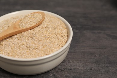 Photo of Oat bran in bowl and spoon on grey table, closeup. Space for text