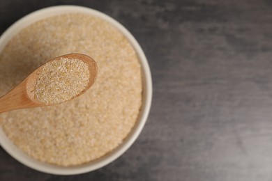 Photo of Oat bran in wooden spoon over bowl at grey table, top view. Space for text