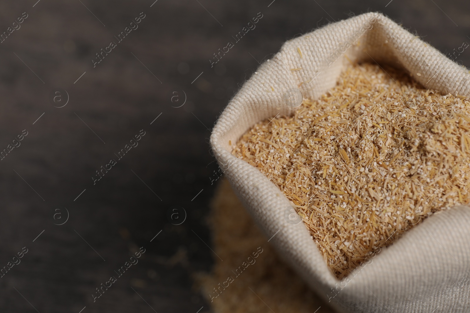 Photo of Oat bran in burlap bag on grey table, closeup. Space for text