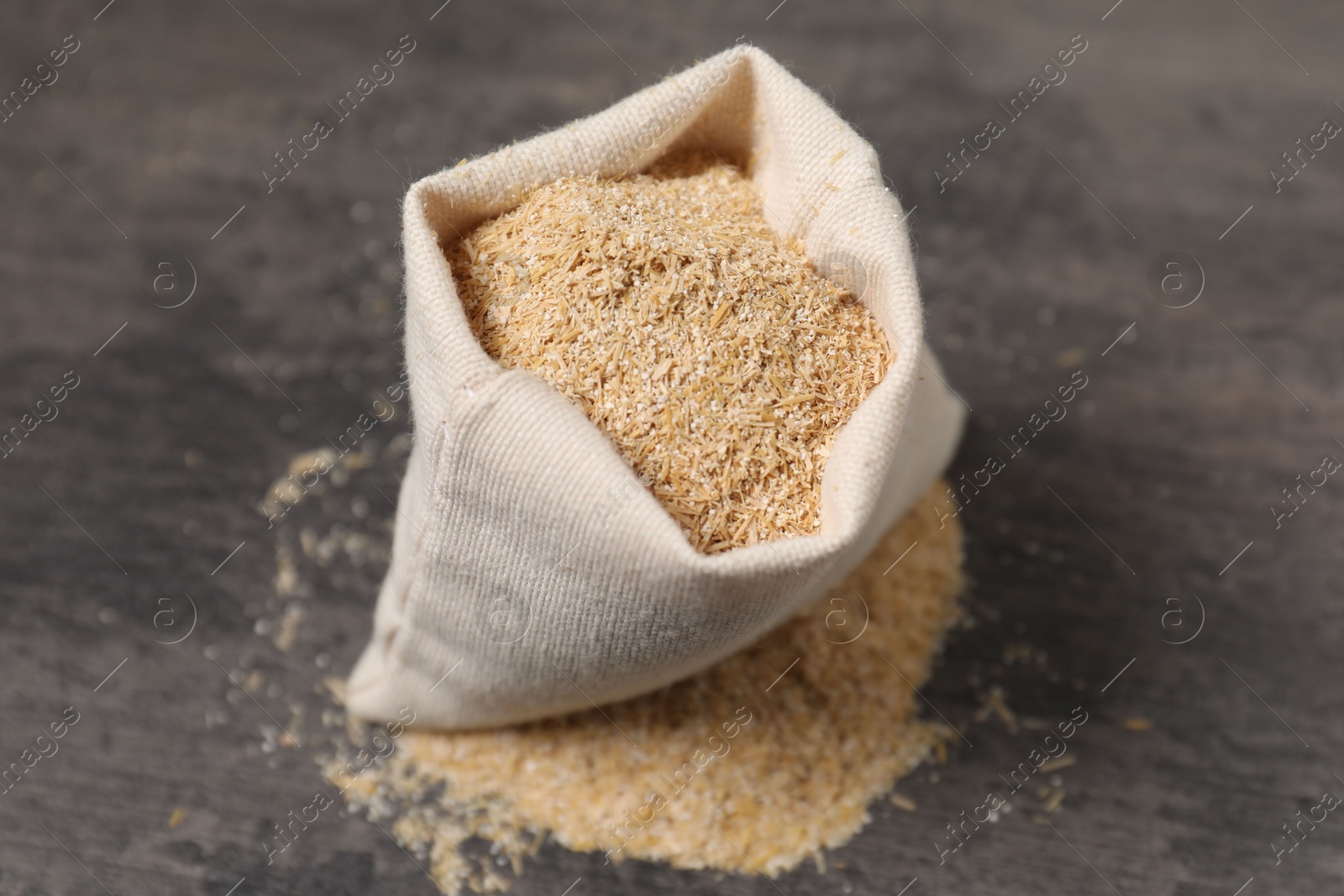 Photo of Oat bran in burlap bag on grey table, closeup