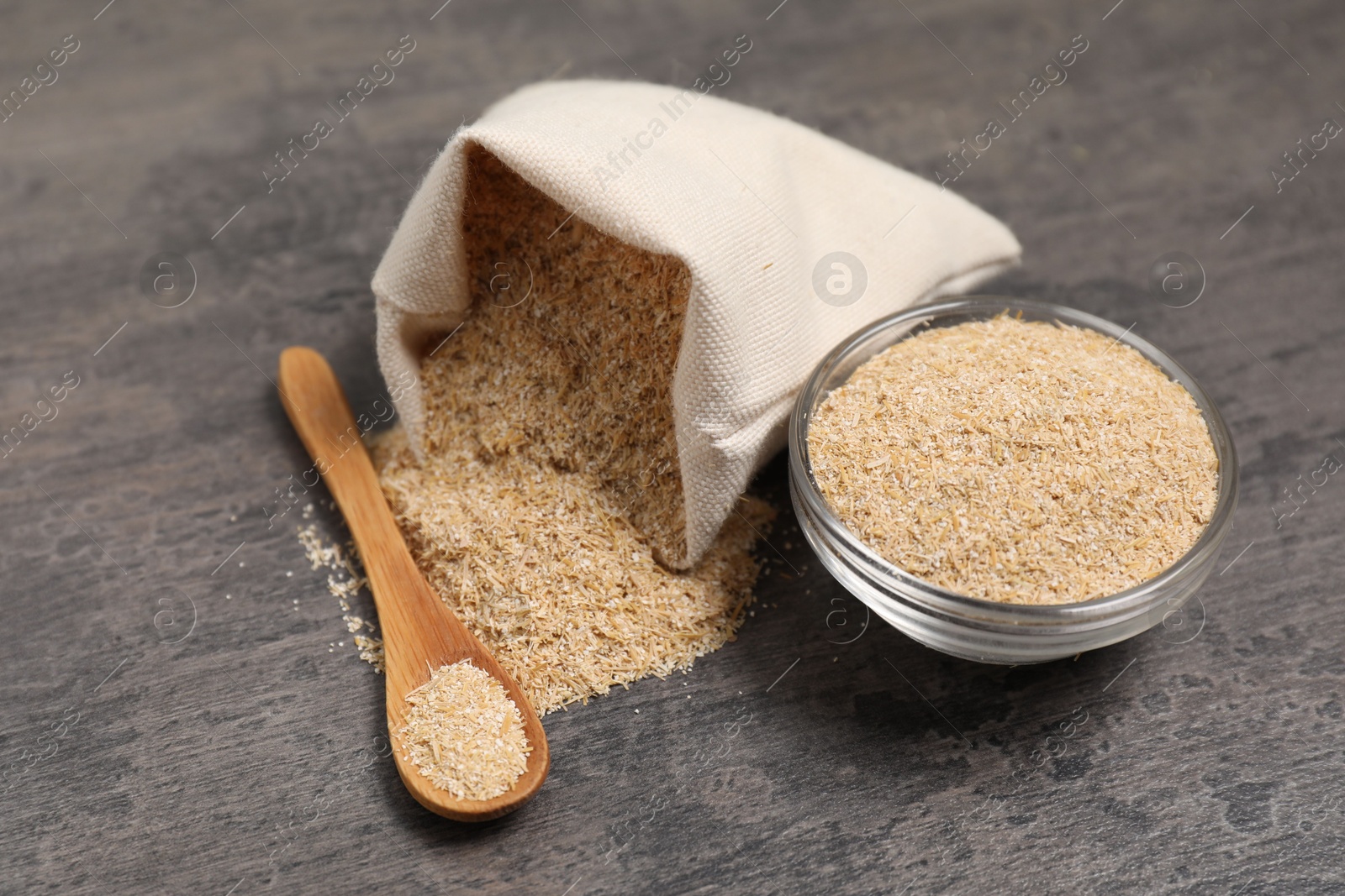 Photo of Oat bran in burlap bag, bowl and spoon on grey table, closeup