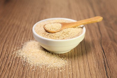 Oat bran in bowl and spoon on wooden table, closeup