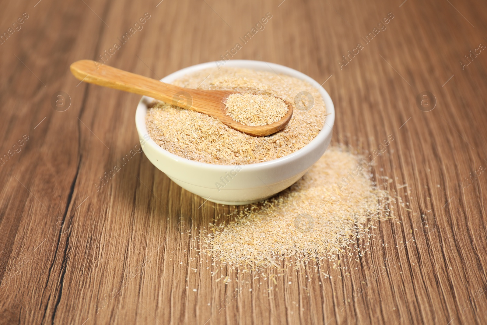 Photo of Oat bran in bowl and spoon on wooden table, closeup