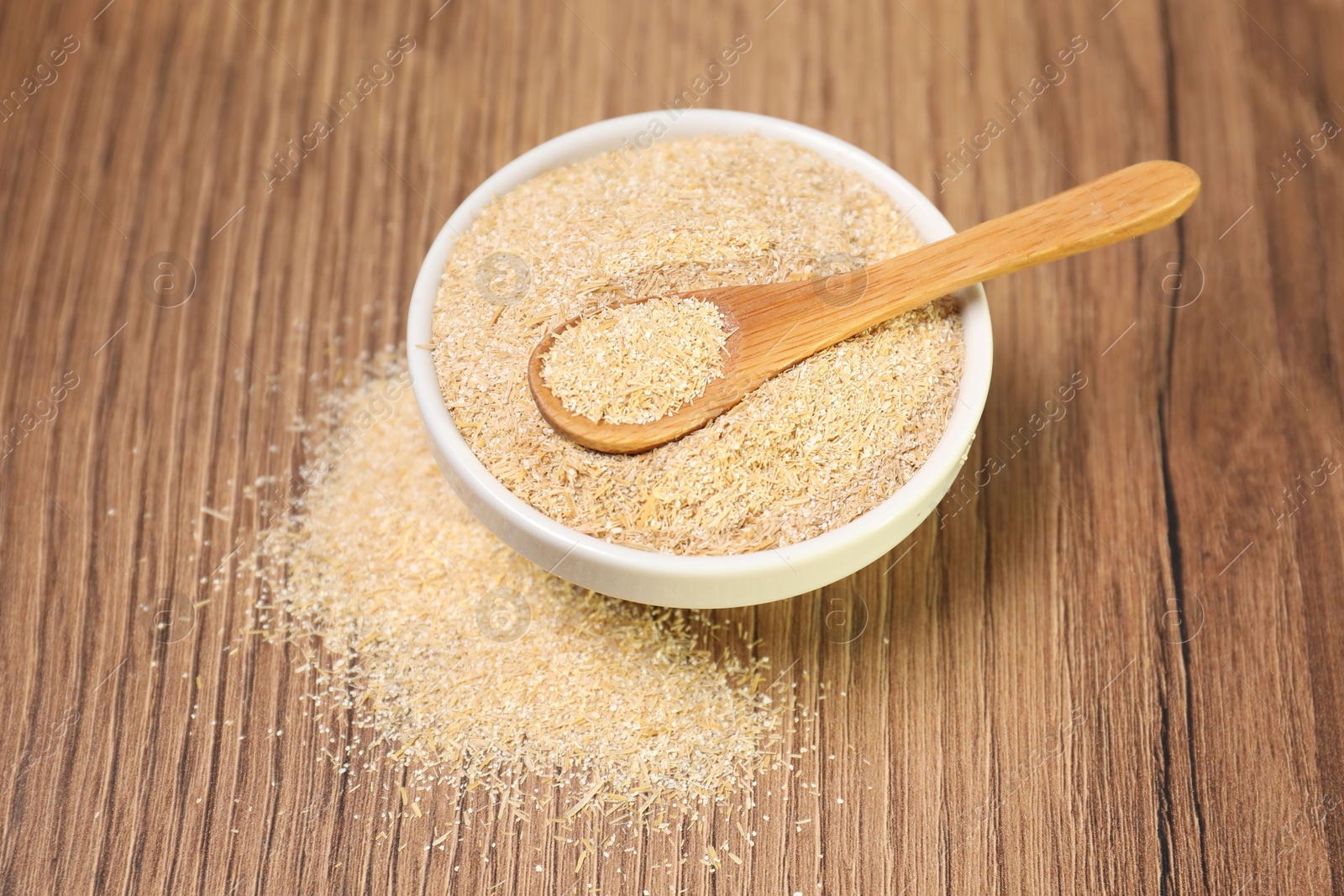 Photo of Oat bran in bowl and spoon on wooden table, closeup