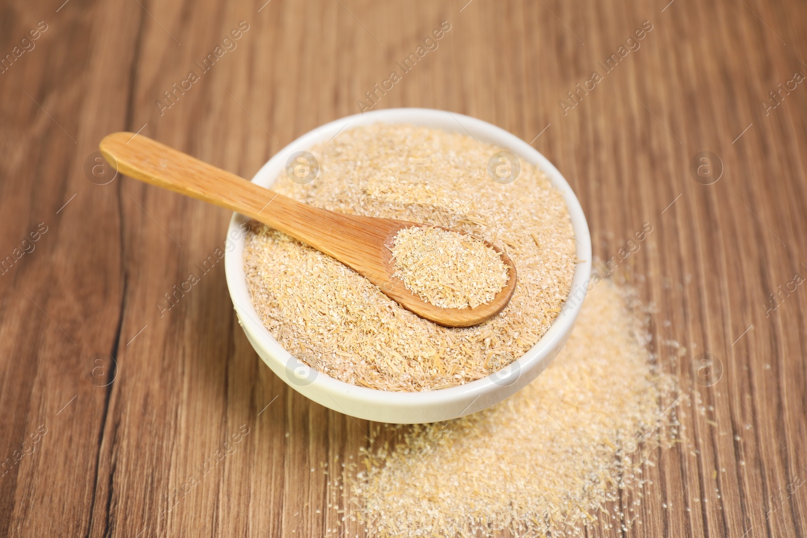 Photo of Oat bran in bowl and spoon on wooden table, closeup