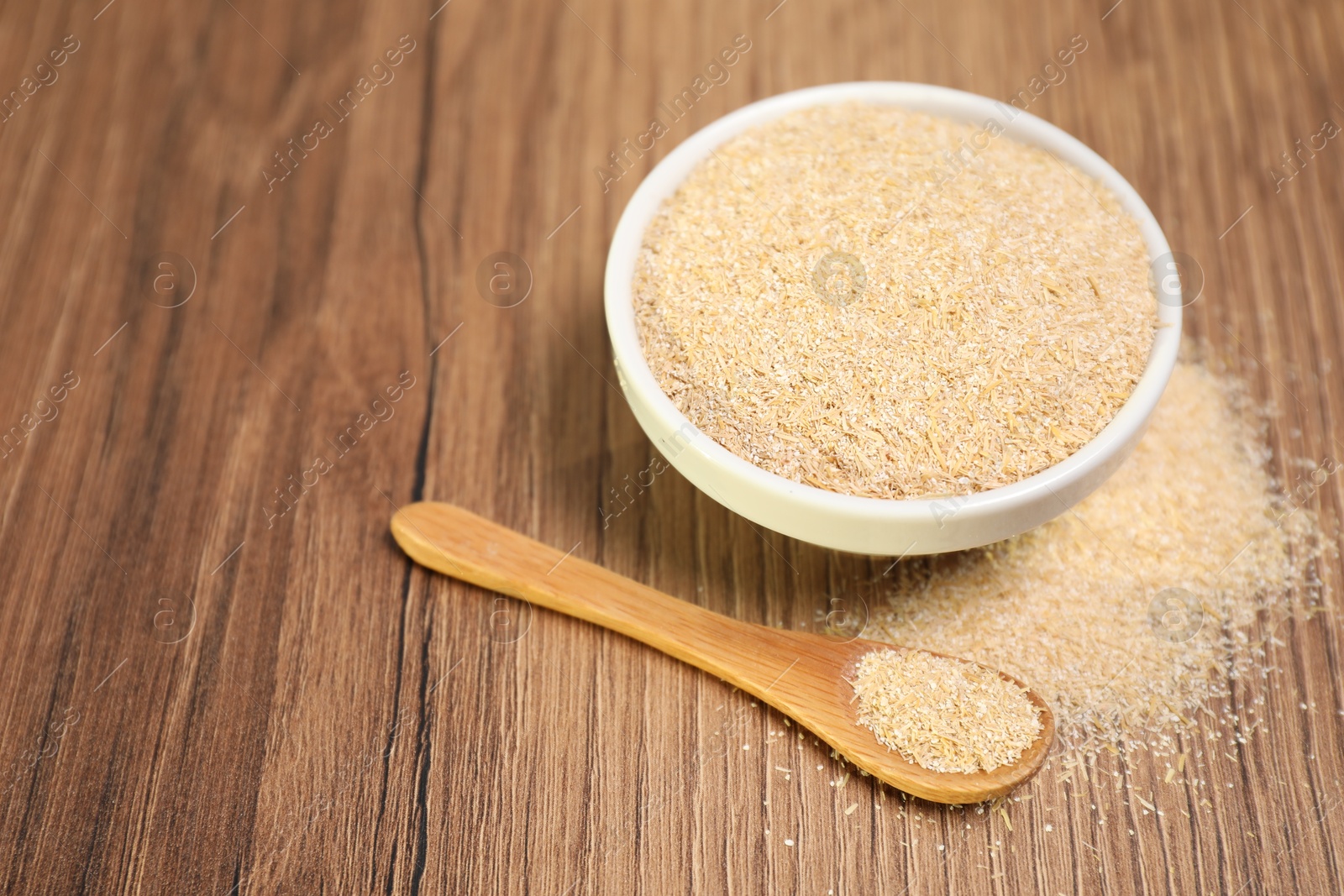 Photo of Oat bran in bowl and spoon on wooden table, closeup