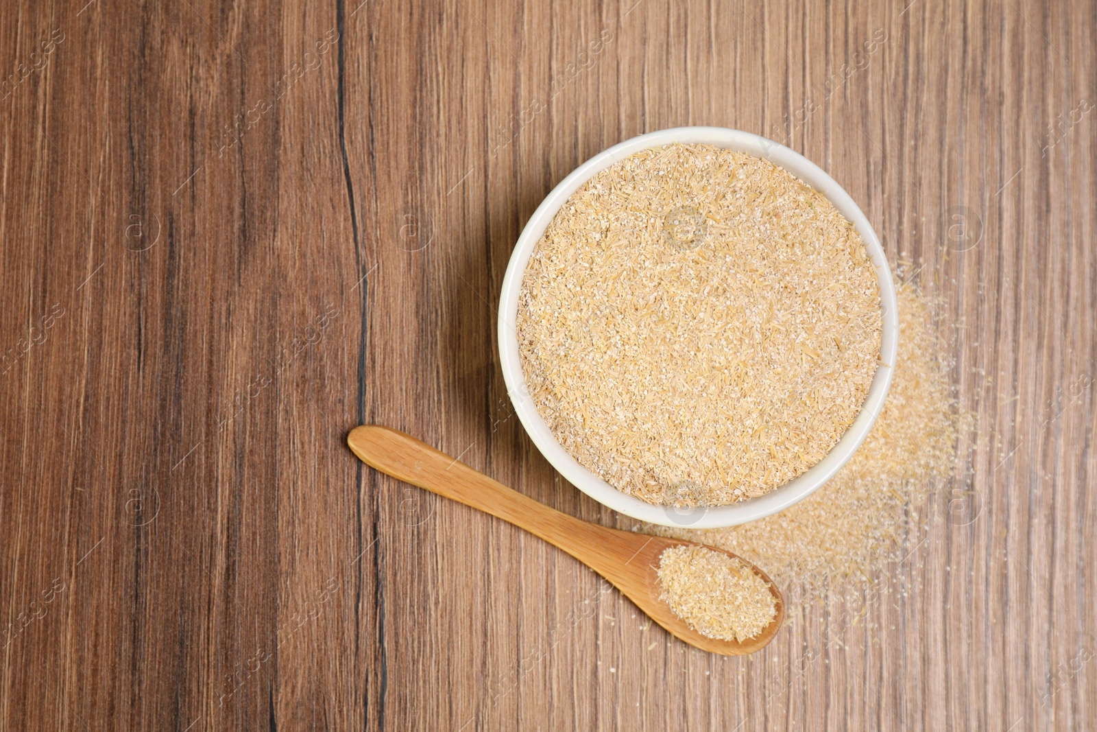 Photo of Oat bran in bowl and spoon on wooden table, top view. Space for text