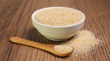 Photo of Oat bran in bowl and spoon on wooden table, closeup