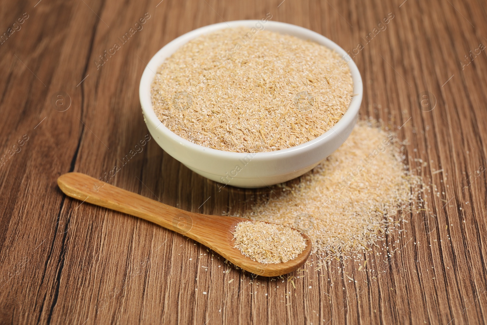 Photo of Oat bran in bowl and spoon on wooden table, closeup