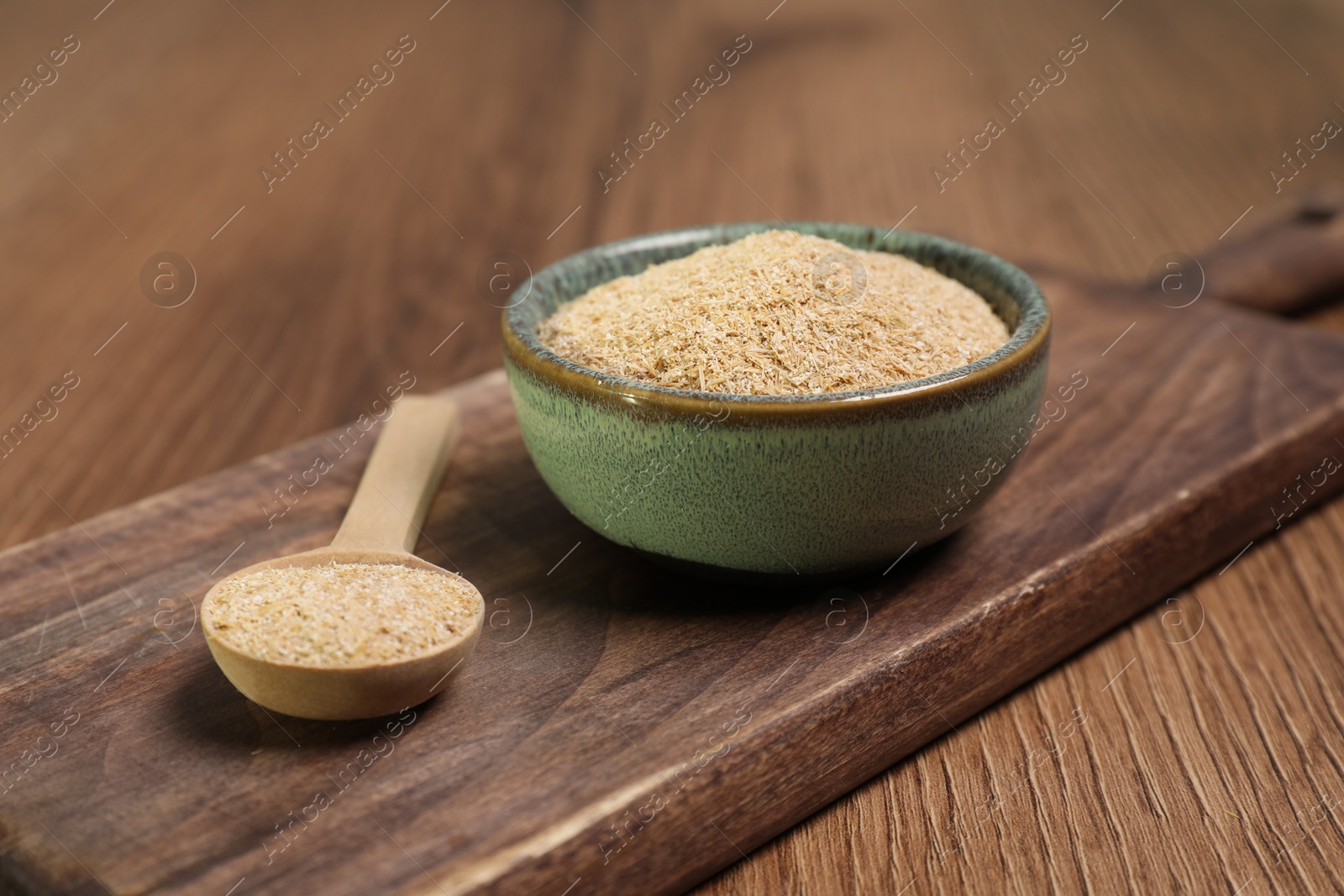 Photo of Oat bran in bowl and spoon on wooden table, closeup