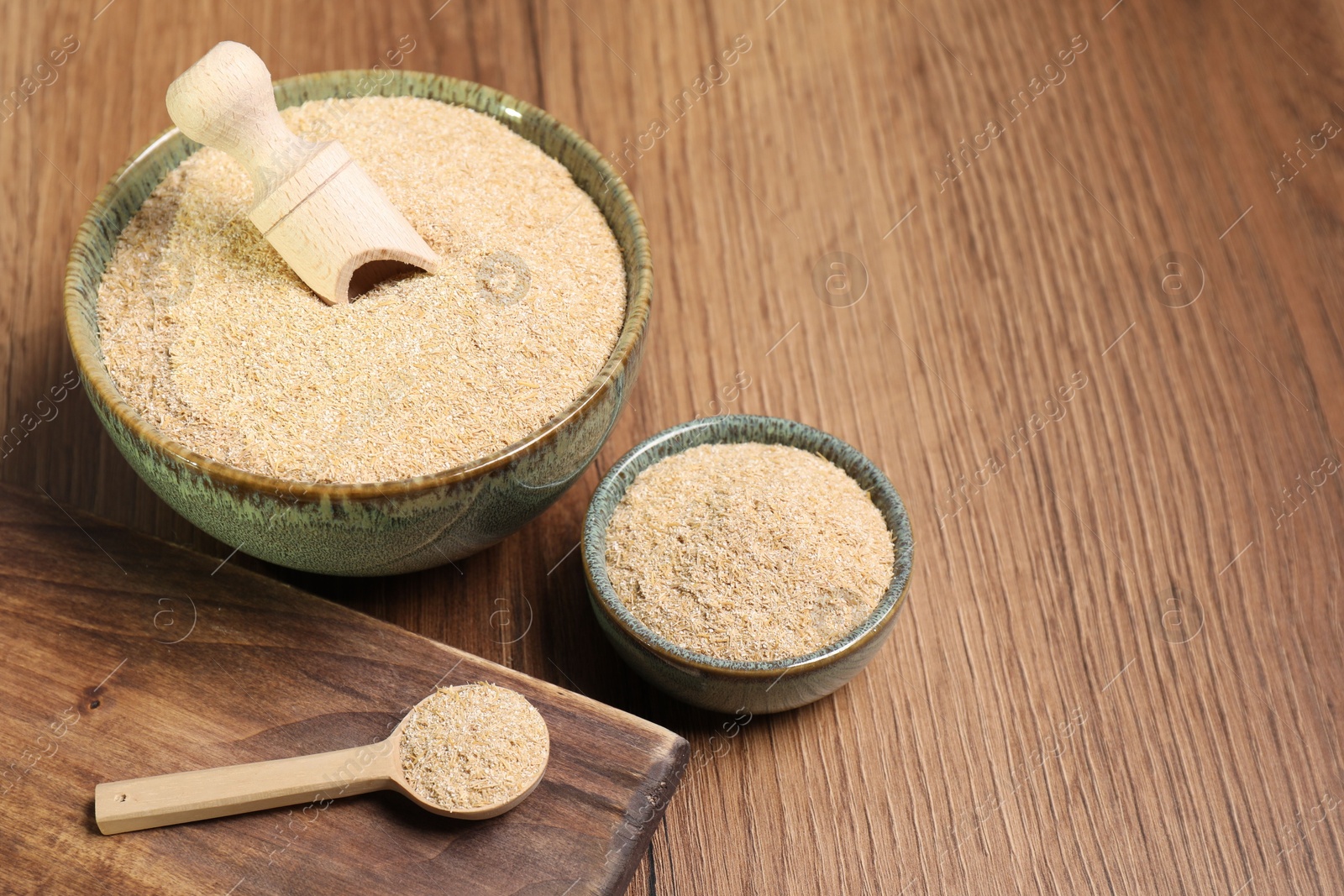 Photo of Oat bran in bowls, spoon and scoop on wooden table, space for text