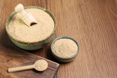 Photo of Oat bran in bowls, spoon and scoop on wooden table, space for text