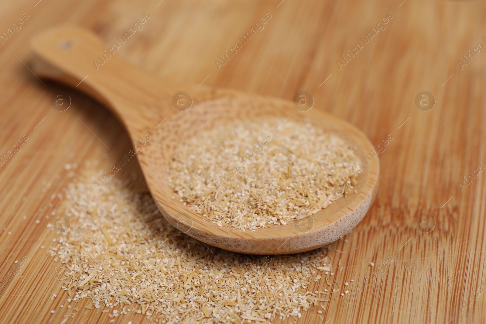 Photo of Oat bran in spoon on wooden table, closeup