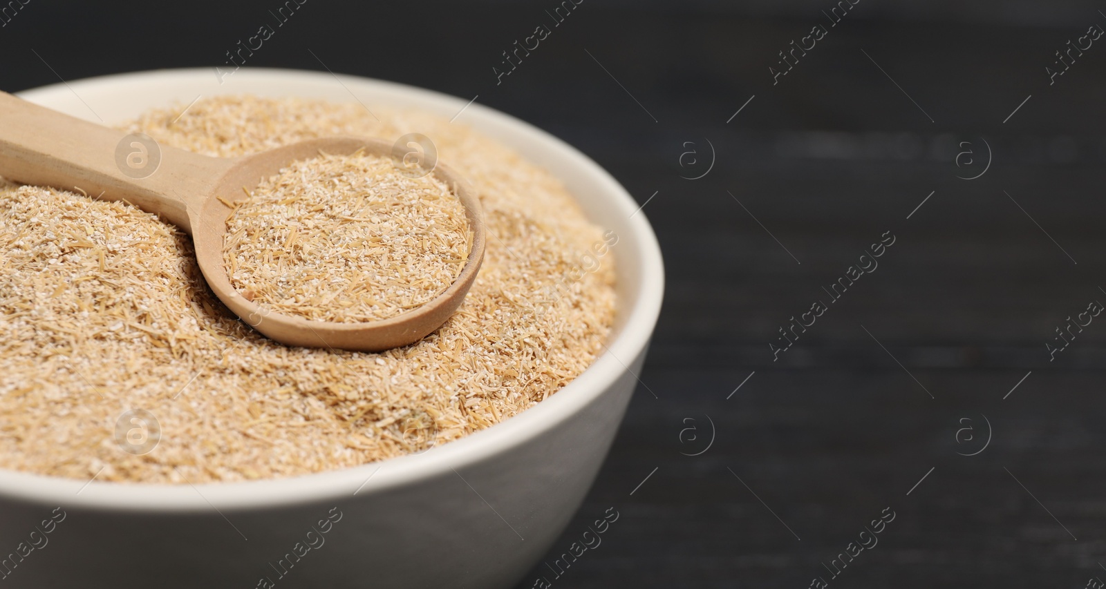 Photo of Oat bran in bowl and spoon on black table, closeup. Space for text